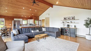 A spacious living room with a large sectional sofa, a wooden ceiling, and a kitchen in the background.