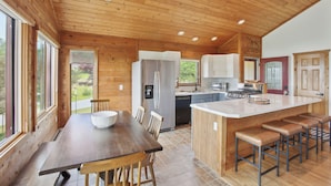 A modern kitchen with wooden walls, a central island with bar stools, and a dining area with a large table and chairs.