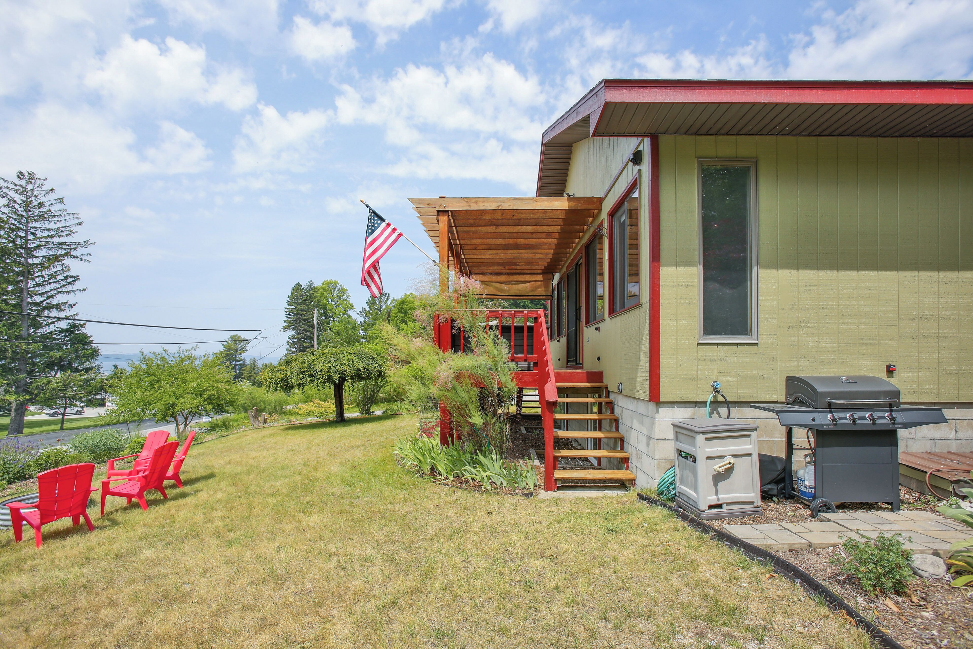 Une maison avec un porche couvert, un barbecue et des chaises rouges.