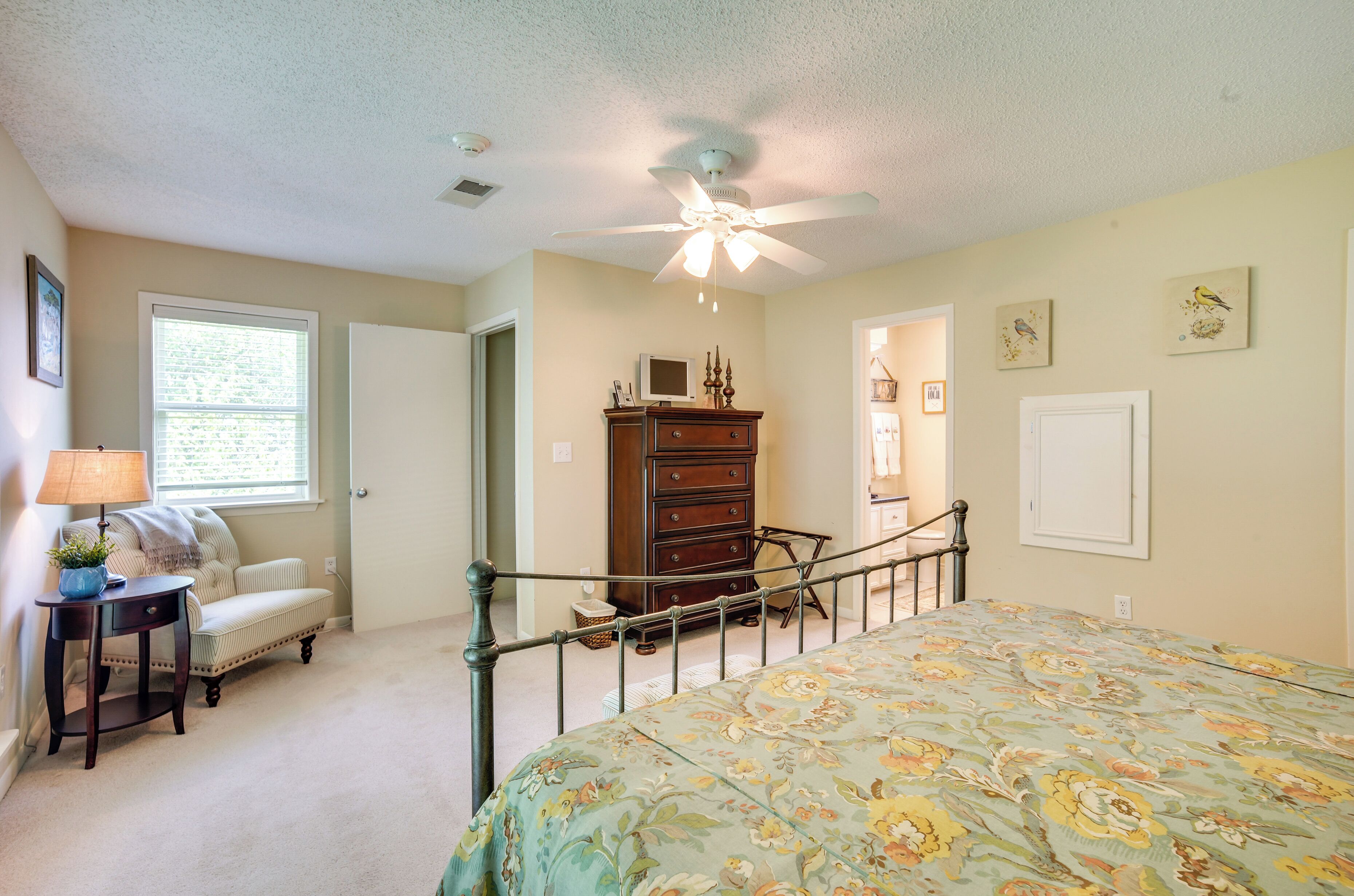 A bedroom with a bed, a dresser, a nightstand, a ceiling fan, and a window with blinds.