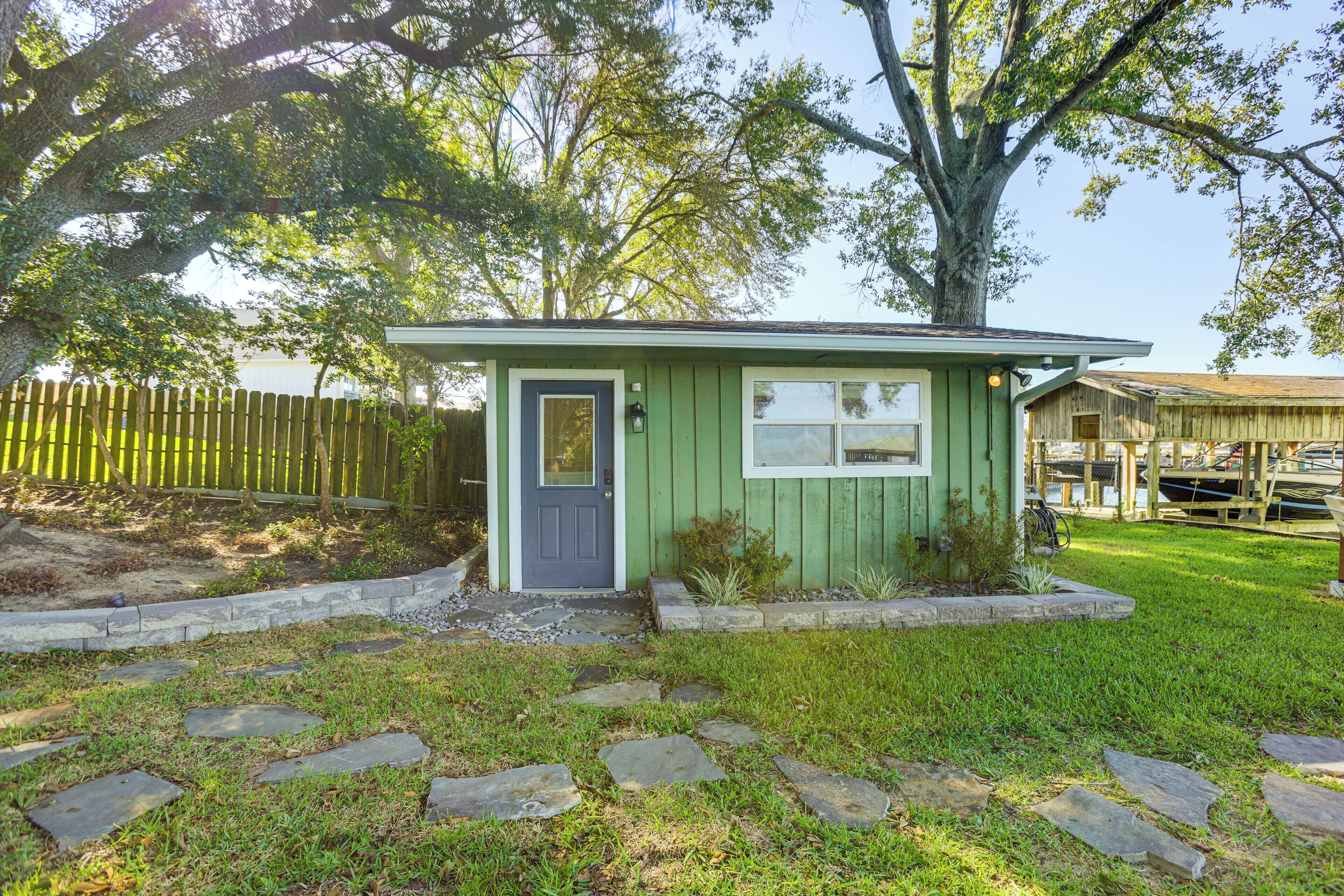 A small, single-story house with a green exterior and a gray door, surrounded by a stone pathway and a wooden fence.
