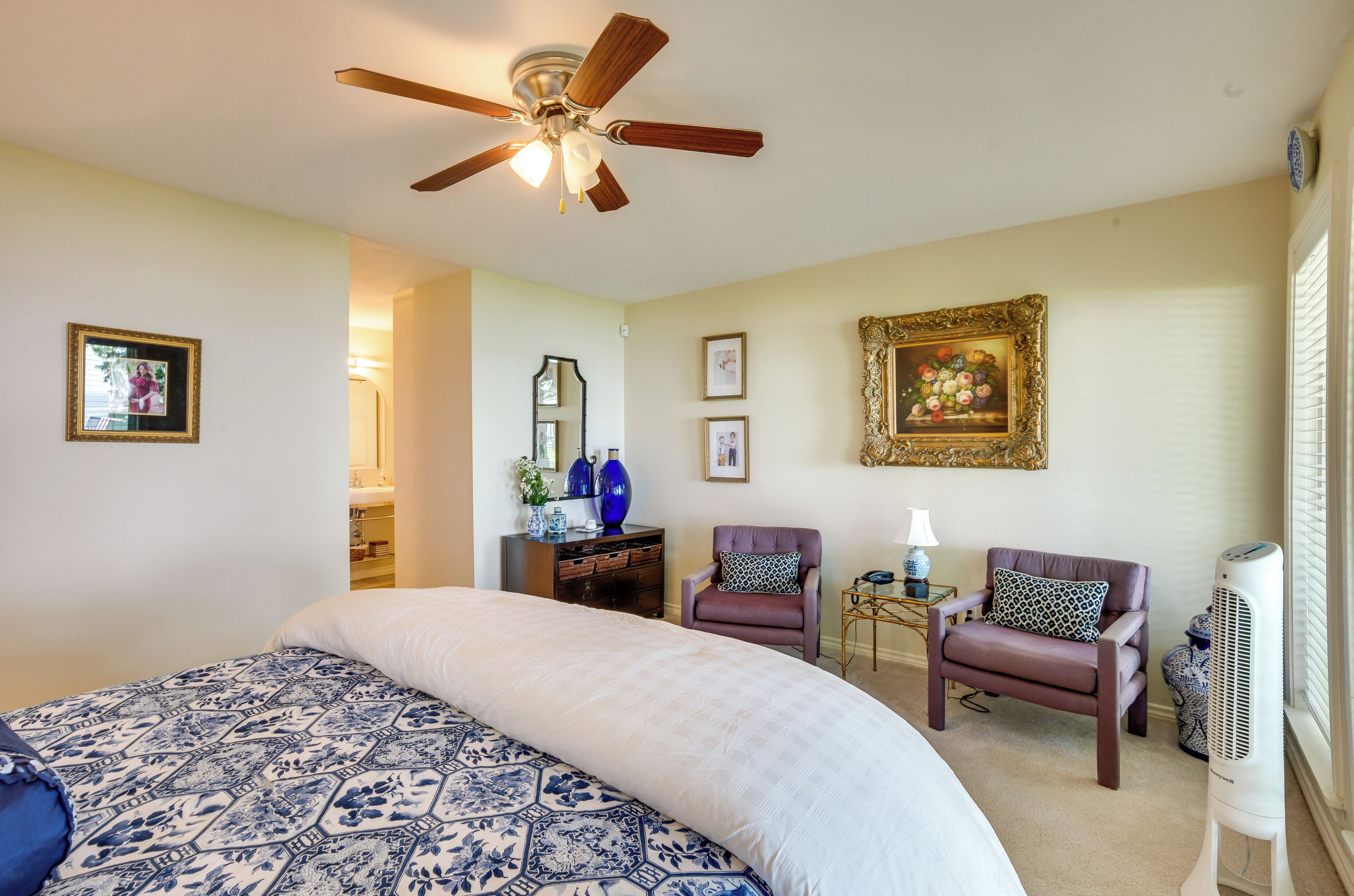 Une chambre à coucher comprenant un lit, deux chaises, une commode, un miroir et un ventilateur de plafond.