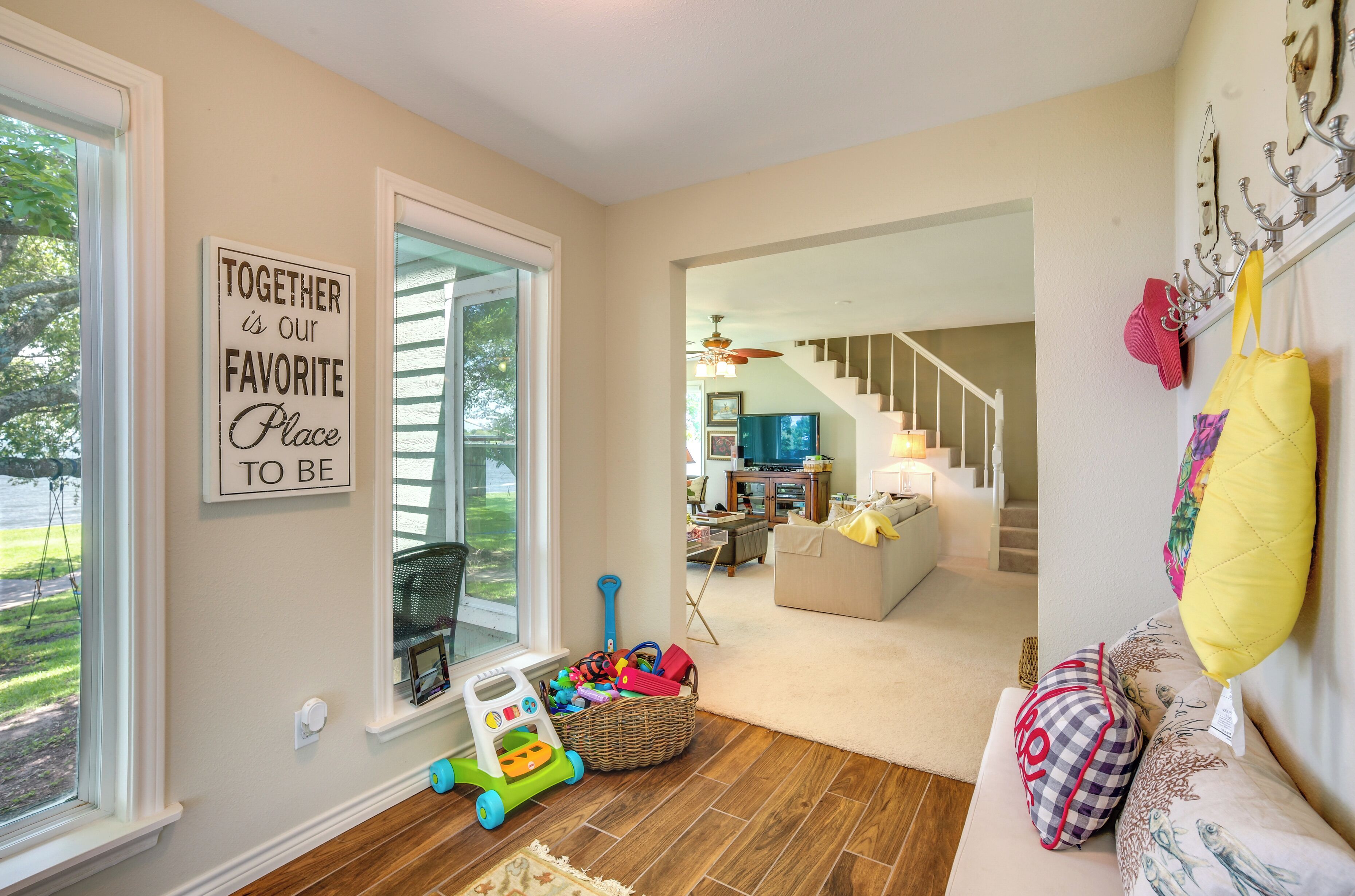 A spacious living room with a large window, a staircase leading to another level, and a cozy seating area with cushions.