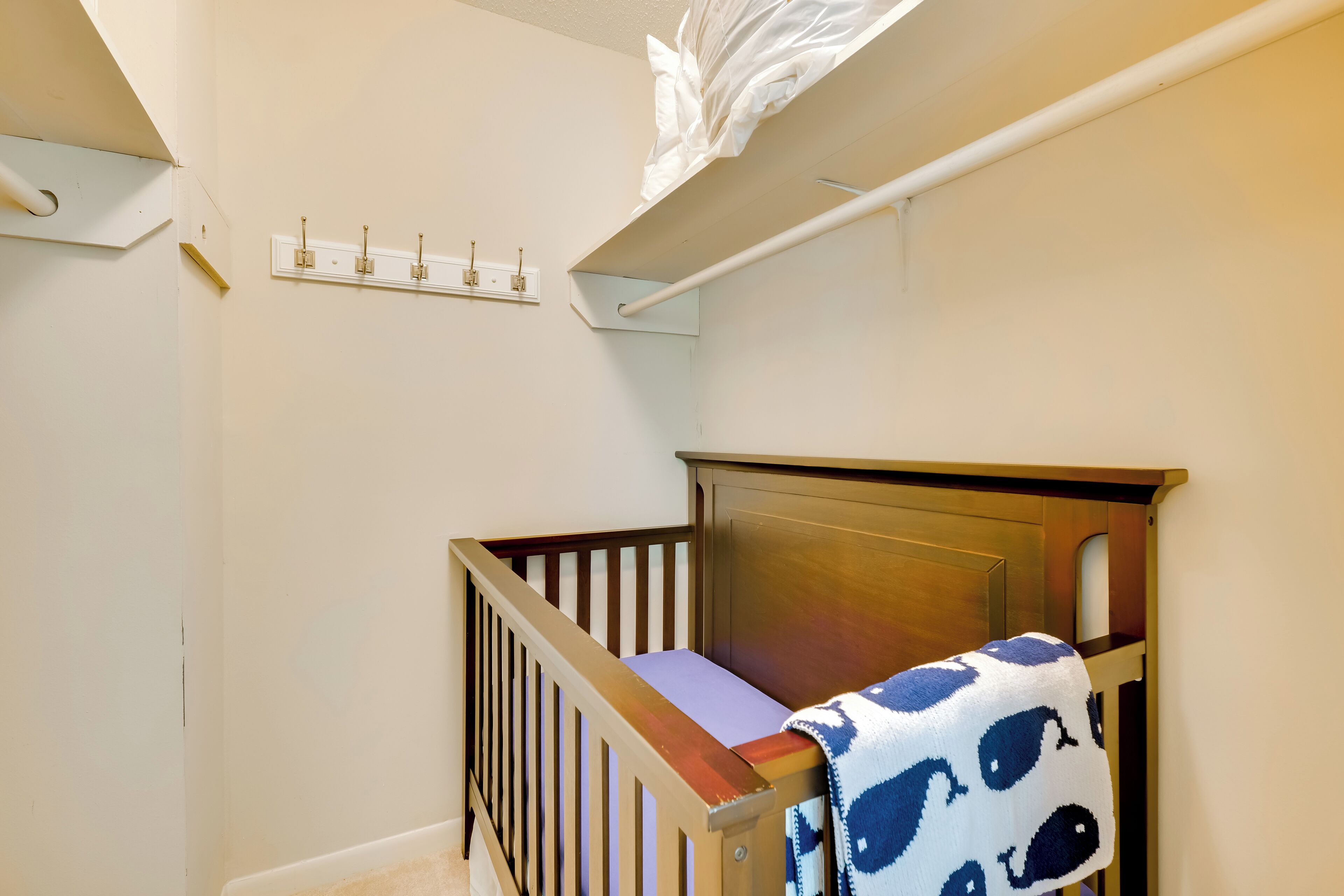 A baby crib with a patterned blanket, a wooden railing, and a white wall with a light switch and electrical outlet.