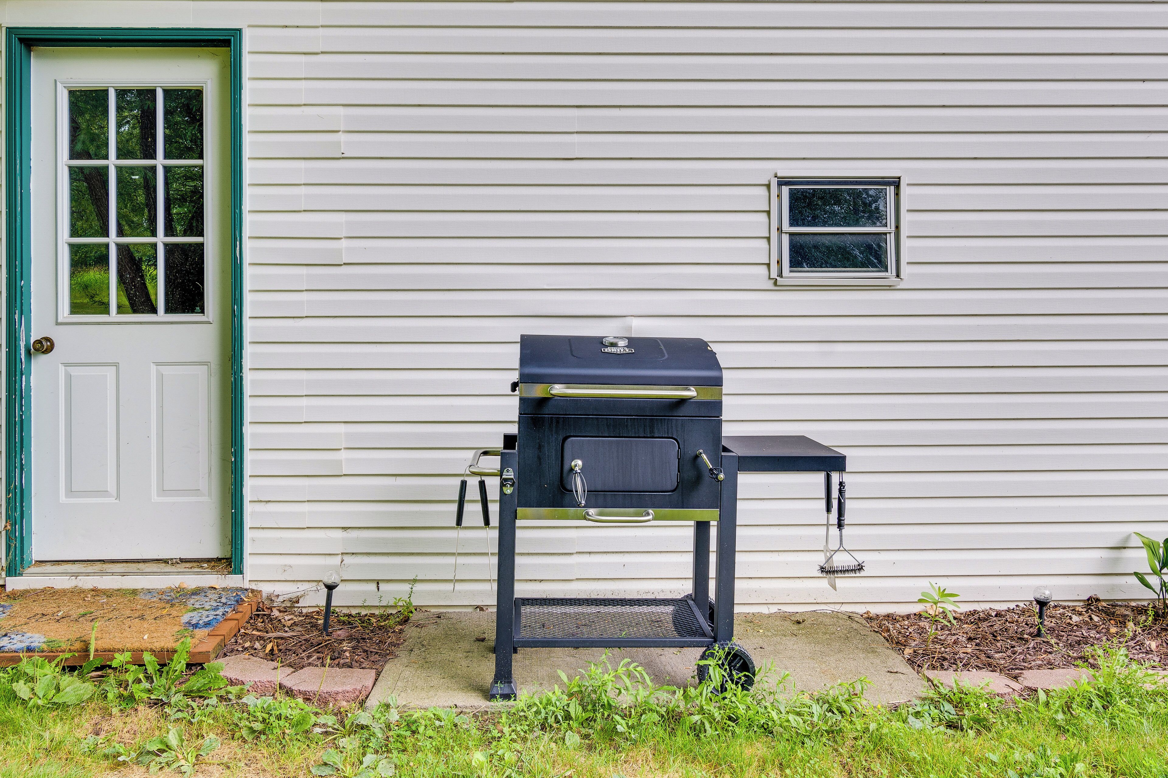A barbecue grill in front of a house with a green door and a small window.