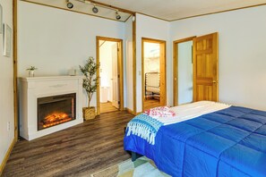 A bedroom with a fireplace, wooden floors, a bed with a blue blanket, and two doors leading to other rooms. - Charming Watkins Glen Home w/ Deck & Yard! (Watkins Glen)