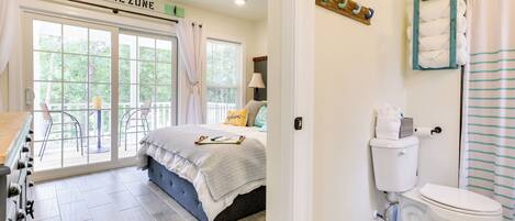 A bedroom with a large window, a bed, a bathroom with a toilet and shower curtain, and a kitchen area with an oven.