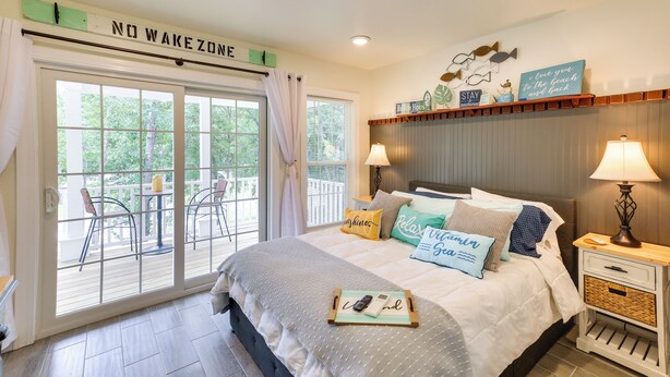 A bedroom with a bed, bedside tables, a nightstand, a window with curtains, and a view of the outdoors. - Cozy Cottage: Minutes to Downtown Southport! (Southport)