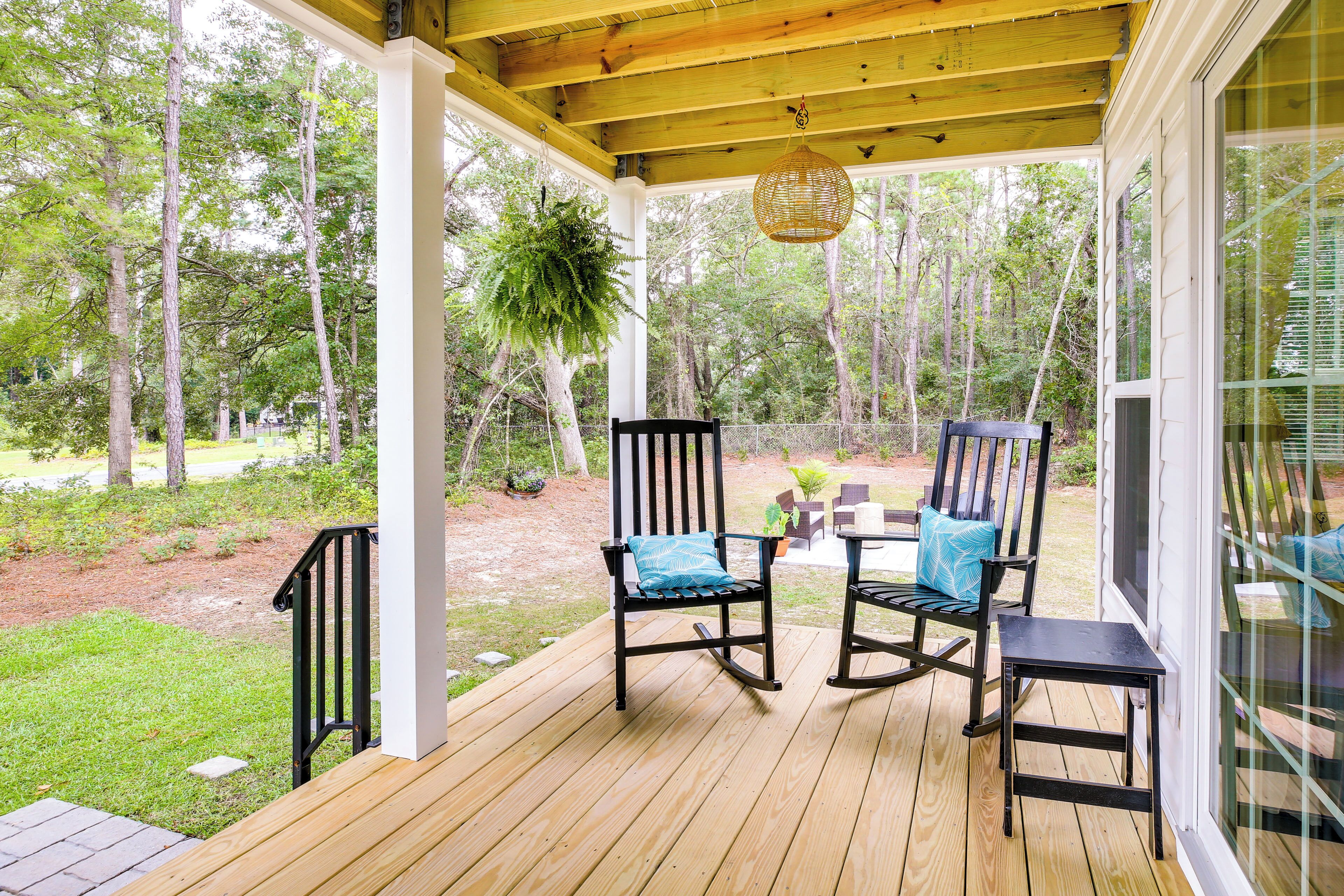 A wooden deck with two rocking chairs and a table, overlooking a forested area.