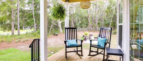 A wooden deck with two rocking chairs and a table, overlooking a forested area.