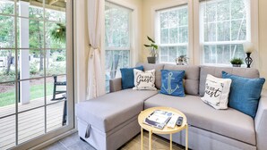 A cozy living room with a sectional sofa, a small round table, and a large window with blinds. - Cozy Cottage: Minutes to Downtown Southport! (Southport)
