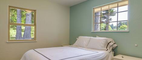 A bedroom with a bed, two windows, a nightstand, and a cabinet.
