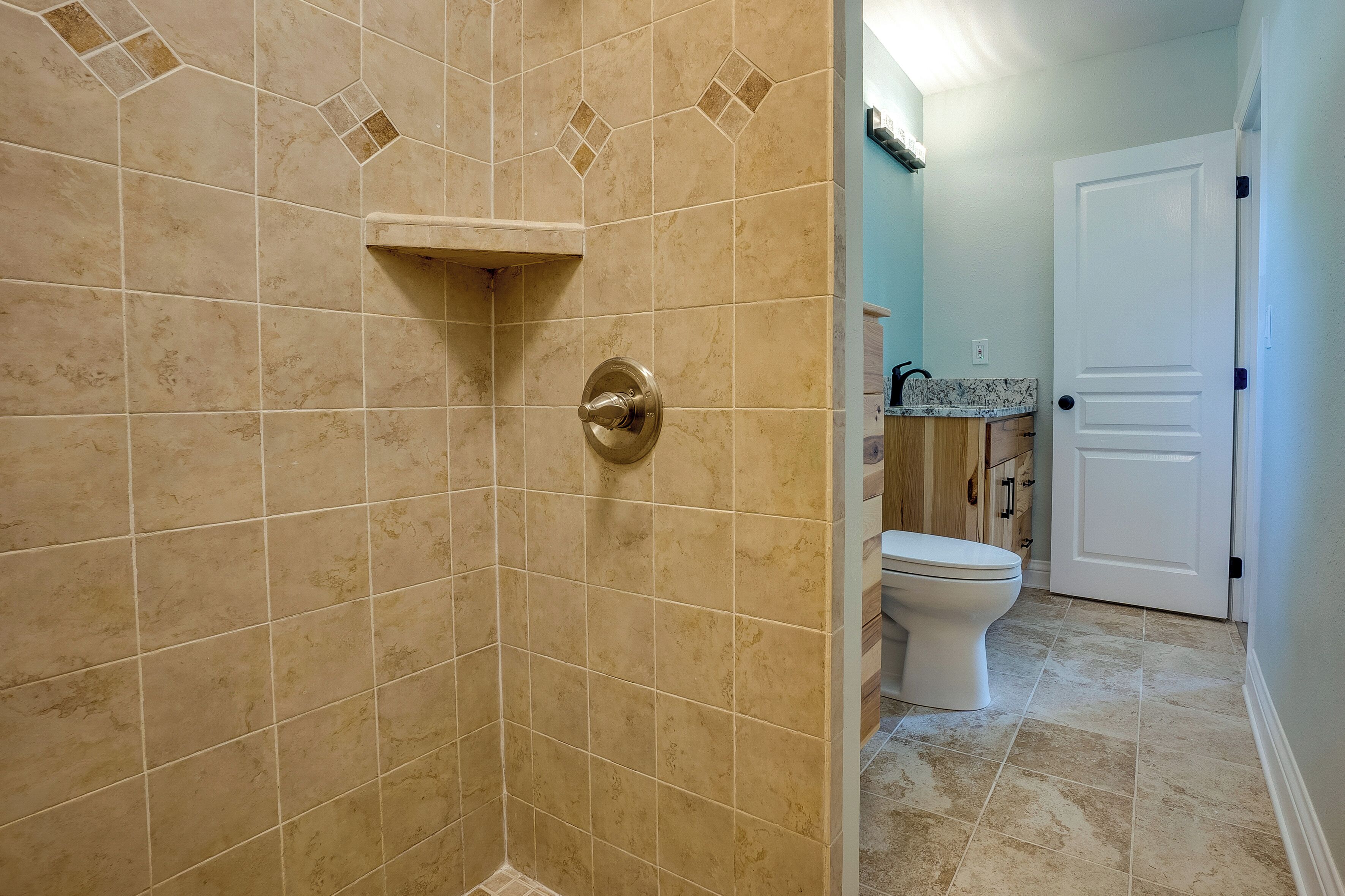 Een badkamer met beige tegels, een douche, een toilet en een deur.