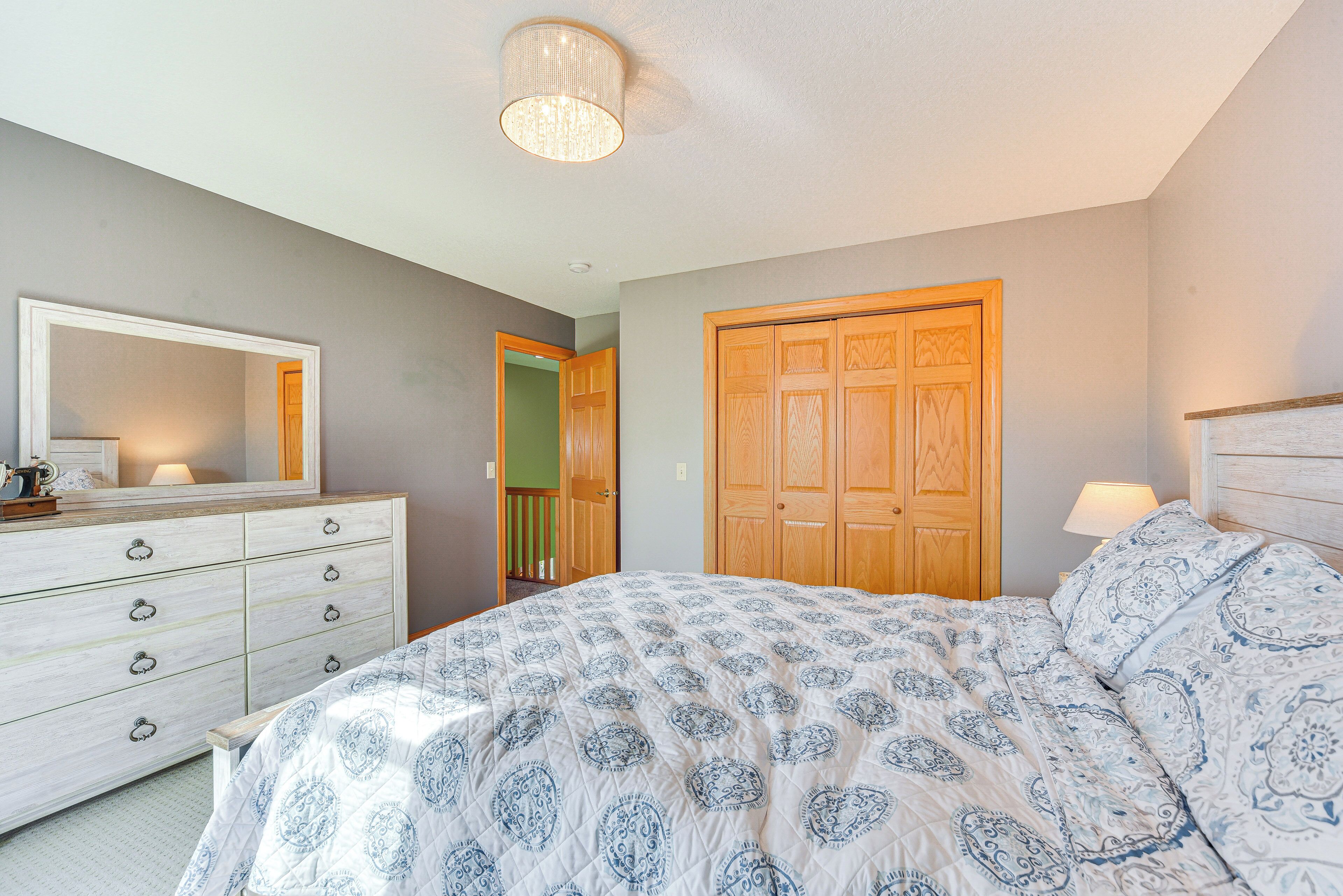 A bedroom with a bed, dresser, mirror, and wooden wardrobe.
