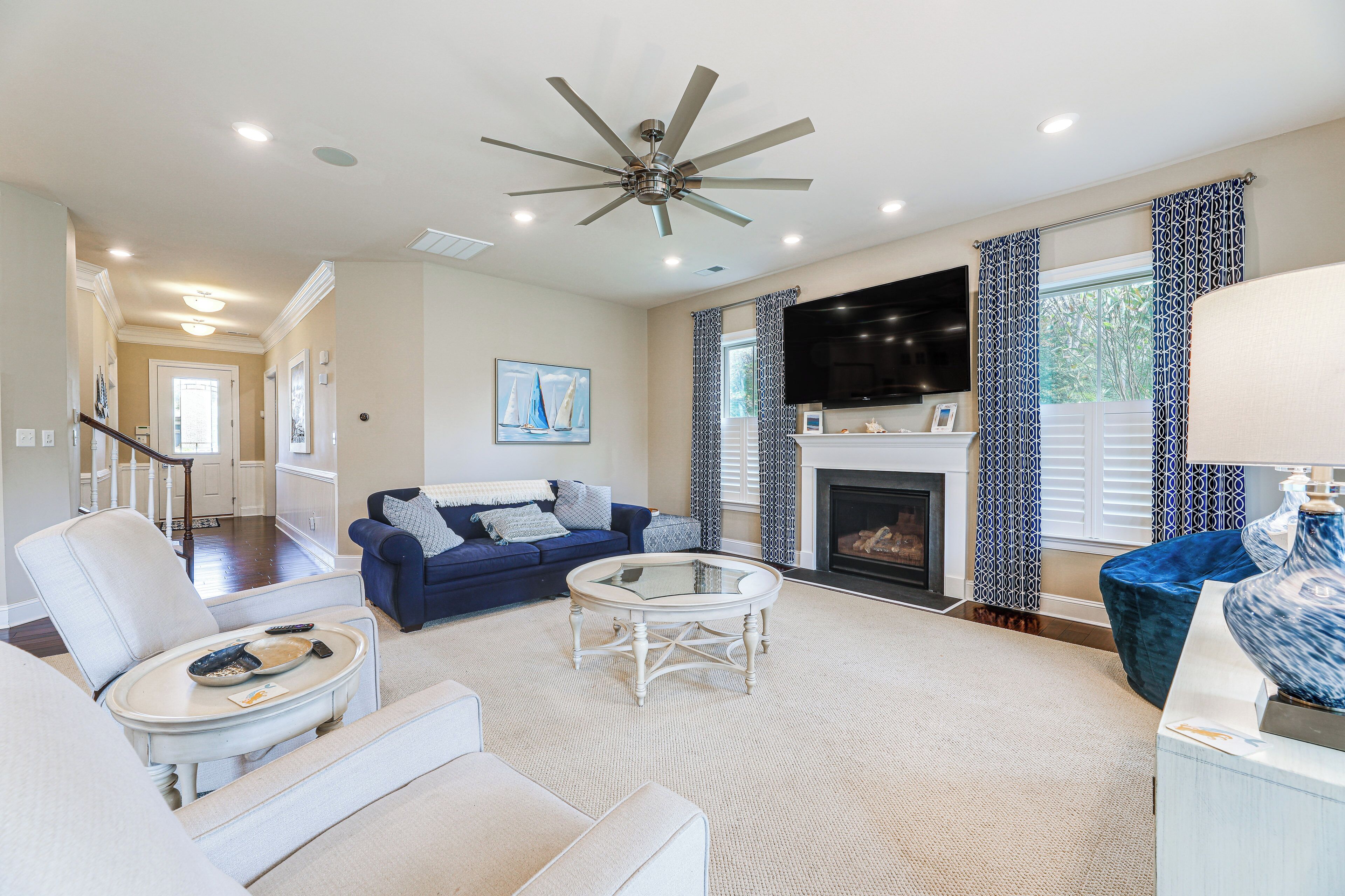 A spacious living room with a ceiling fan, a fireplace, a TV, and a large window with patterned curtains.
