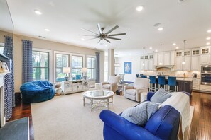 A spacious living room with a blue sofa, a glass coffee table, and a ceiling fan.