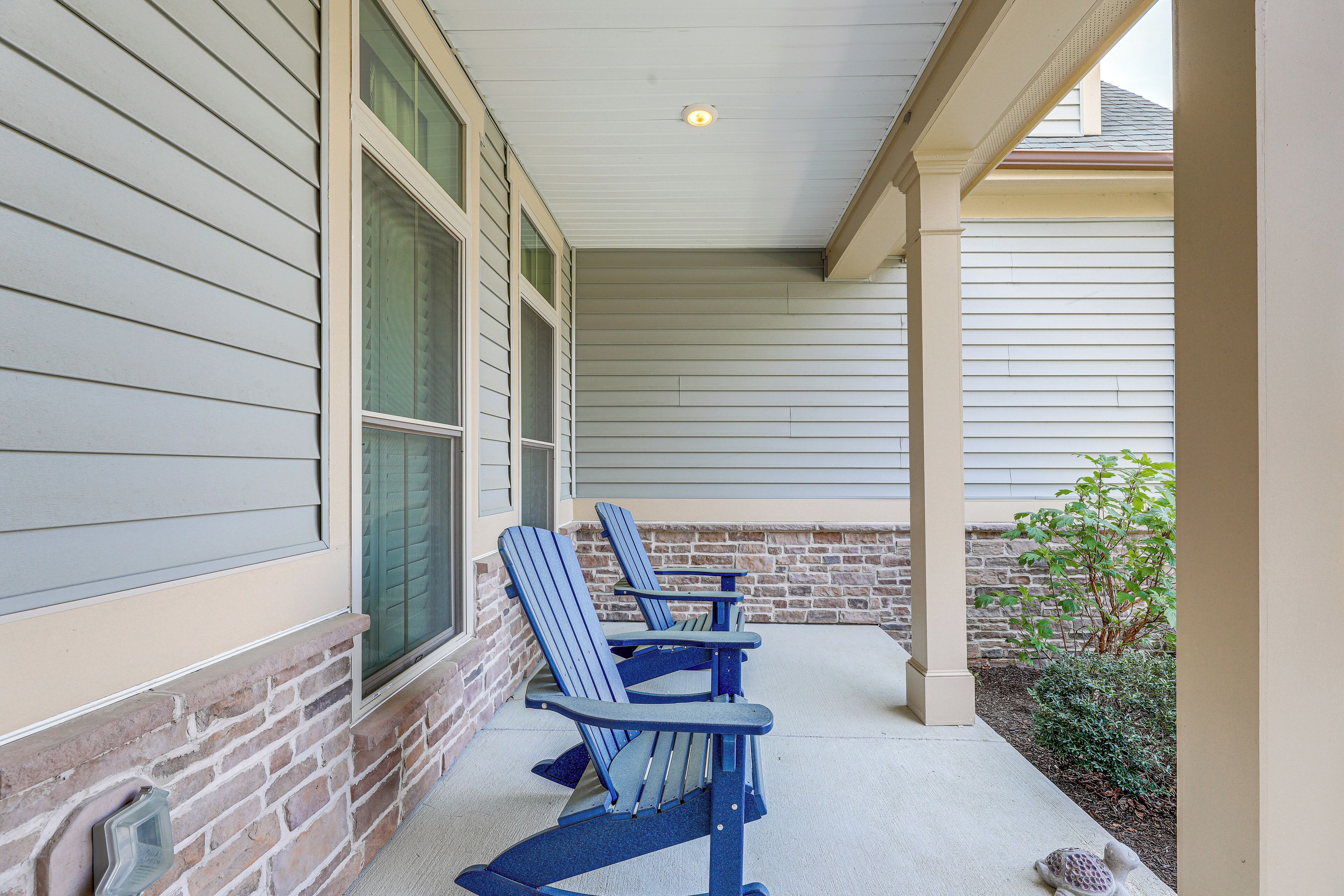 A covered porch with two Adirondack chairs and a small turtle on the ground.