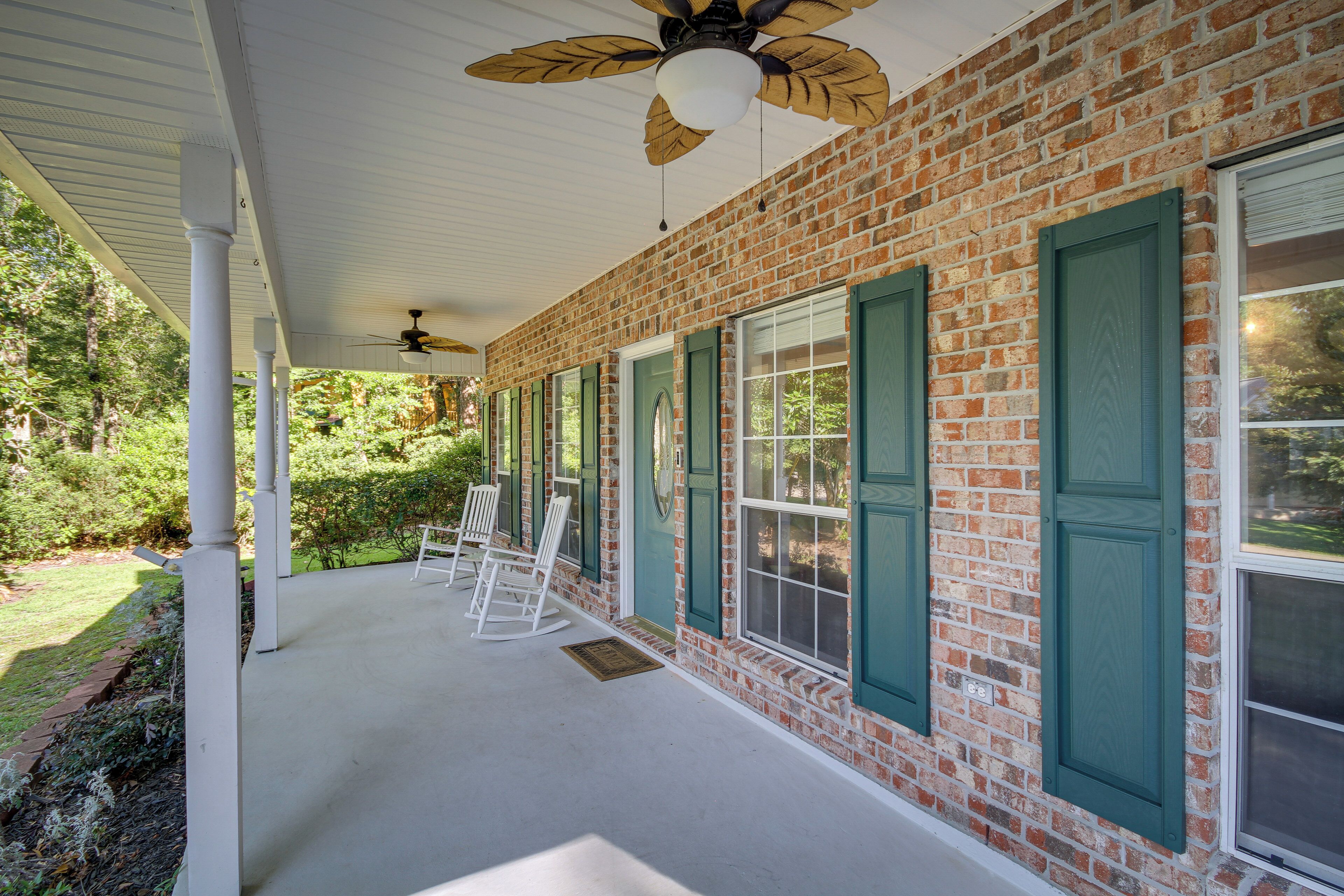 A covered porch with brick walls, green shutters, and white columns.