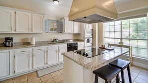 A kitchen with white cabinets, a granite countertop, a central island with stools, and a large window providing natural light. - Charming Diamondhead Home w/ Private Yard! (Diamondhead)