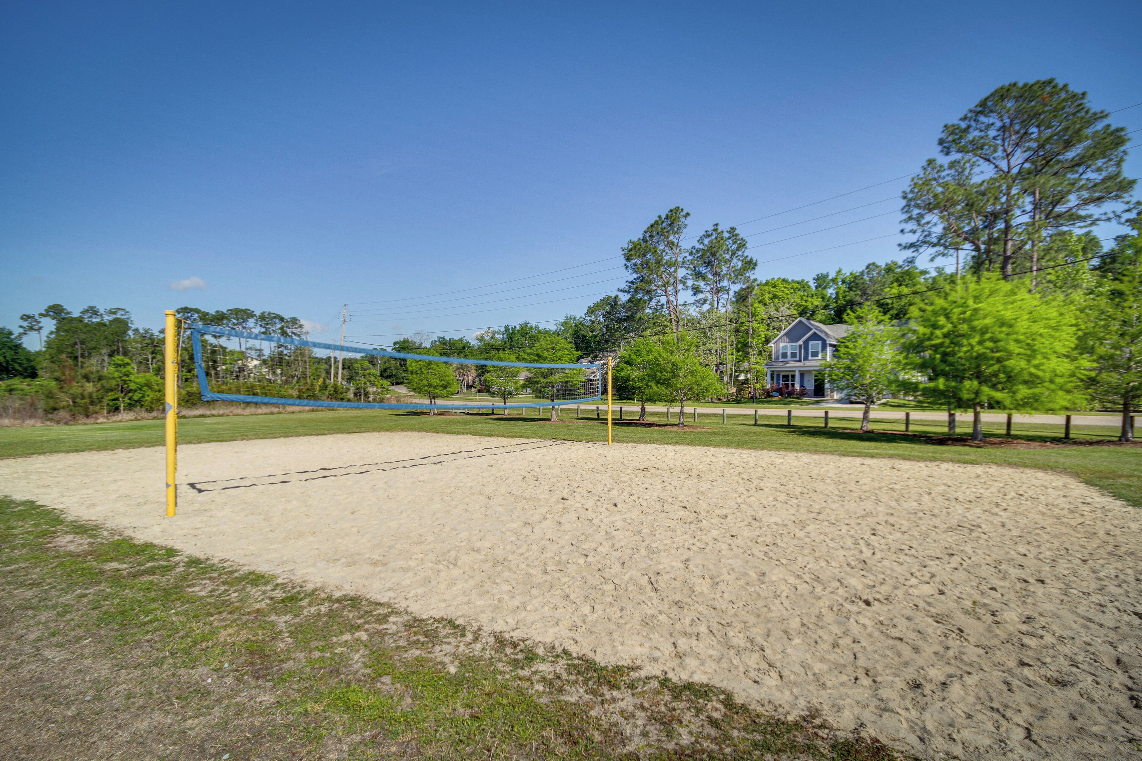 Volleyball court amb una xarxa, envoltat de sorra i gespa, i una casa i arbres al fons.