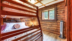 Una habitación tipo cabaña de madera con literas, una ventana con vista a árboles y un calentador.