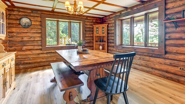 Interior rústico de una cabaña de madera con una mesa de comedor de madera, una silla negra y una araña.