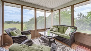Een overdekt terras met rieten meubels, een glazen tafel en uitzicht op een groen landschap.