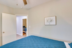 A bedroom with a patterned blue bedspread, a framed artwork on the wall, and a door leading to another room.