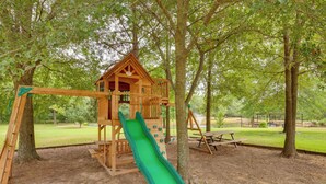 Une structure de jeux en bois avec un toboggan, entourée d’arbres.