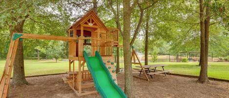 A wooden play structure with a slide, surrounded by trees.