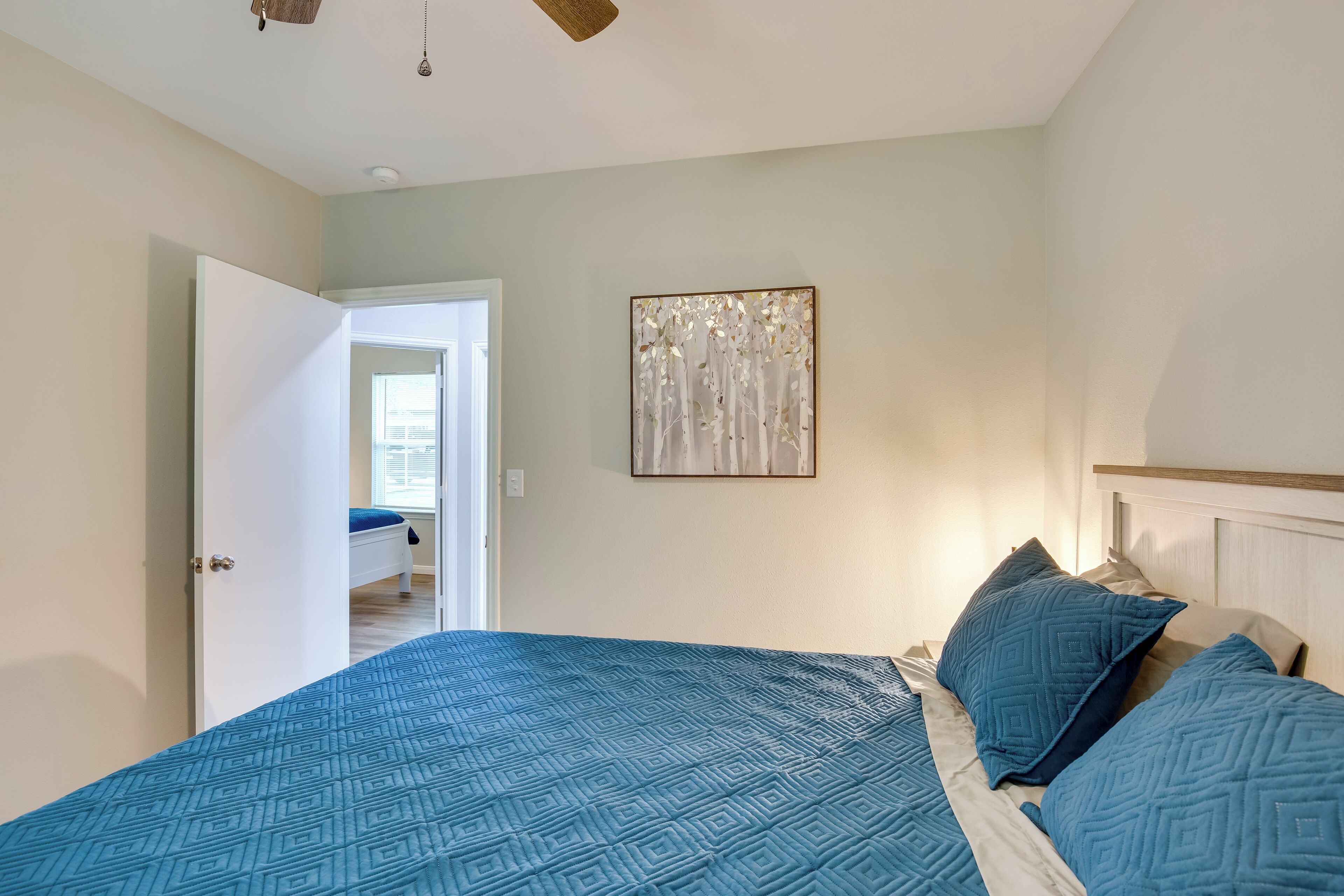 Ein Schlafzimmer mit einem Bett, einer Tür zu einem anderen Raum und einem an der Wand hängenden Kunstwerk.