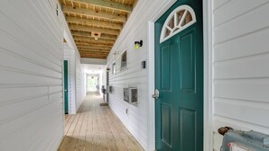 Un pasillo estrecho con pisos de madera y paredes blancas, que conduce a una puerta verde con arco blanco.