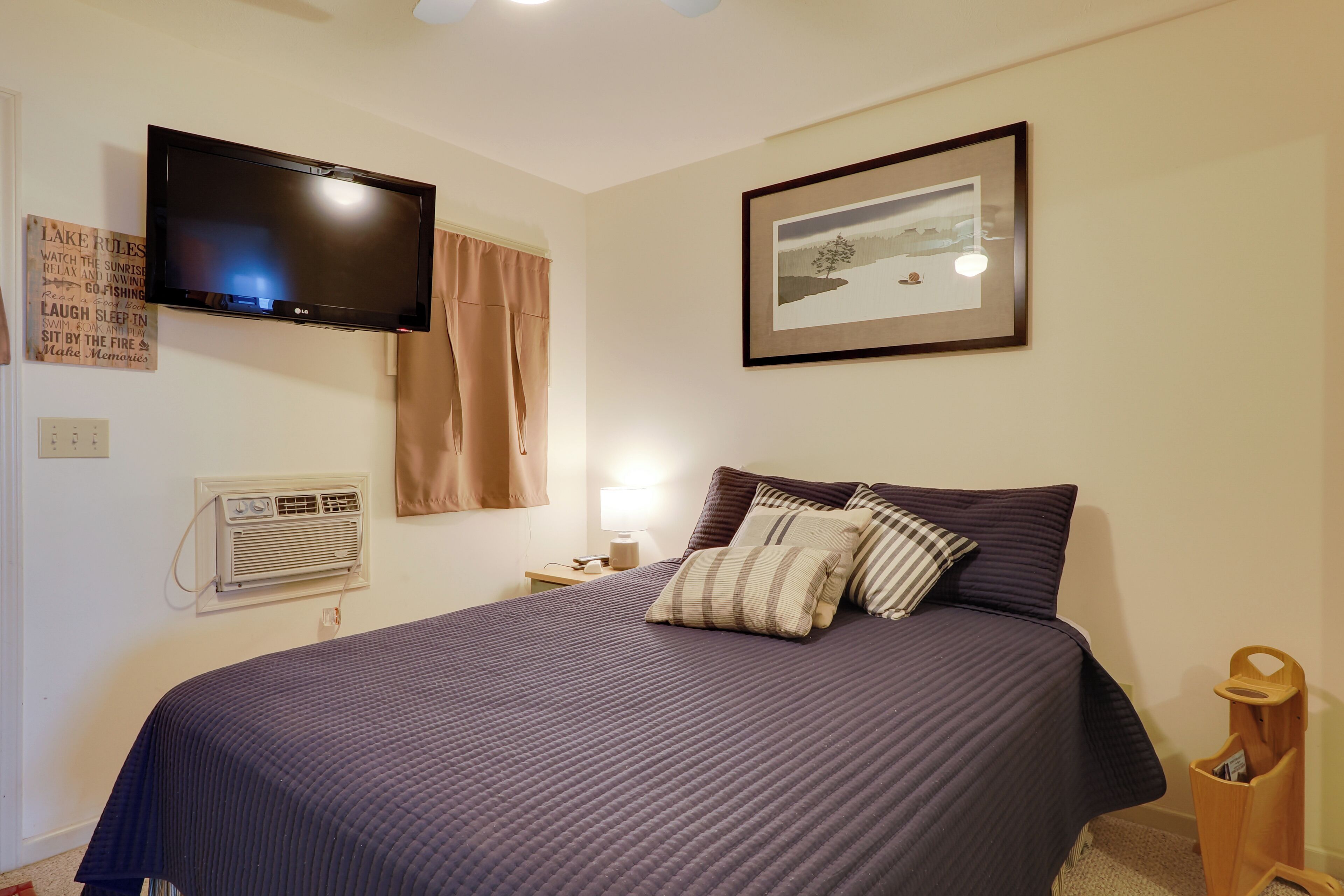 A bedroom with a bed, a television mounted on the wall, a framed picture, and a sign with text.