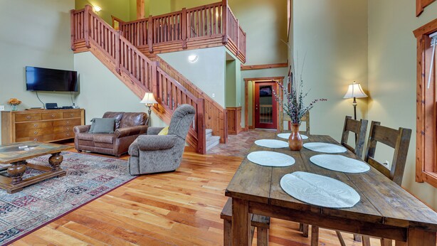 A spacious living room with a wooden staircase, a dining table set with placemats, and a leather sofa. - Slaty Fork Home ~ 6 Mi to Snowshoe Mountain Resort (Snowshoe)