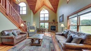 A spacious living room with a high ceiling, wooden staircase, leather sofas, a fireplace, and large windows. - Slaty Fork Home ~ 6 Mi to Snowshoe Mountain Resort (Snowshoe)