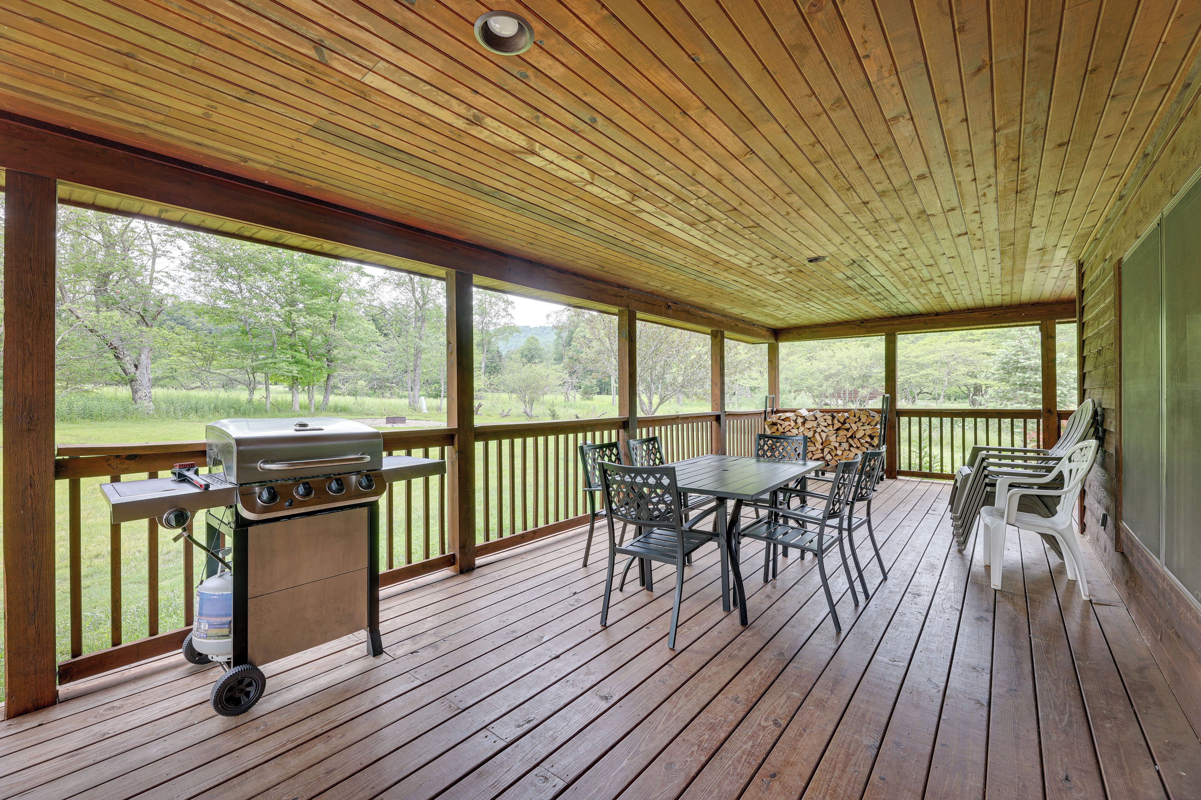 Un patio exterior cubierto con una parrilla, una mesa, sillas y vistas a un espacio con césped.