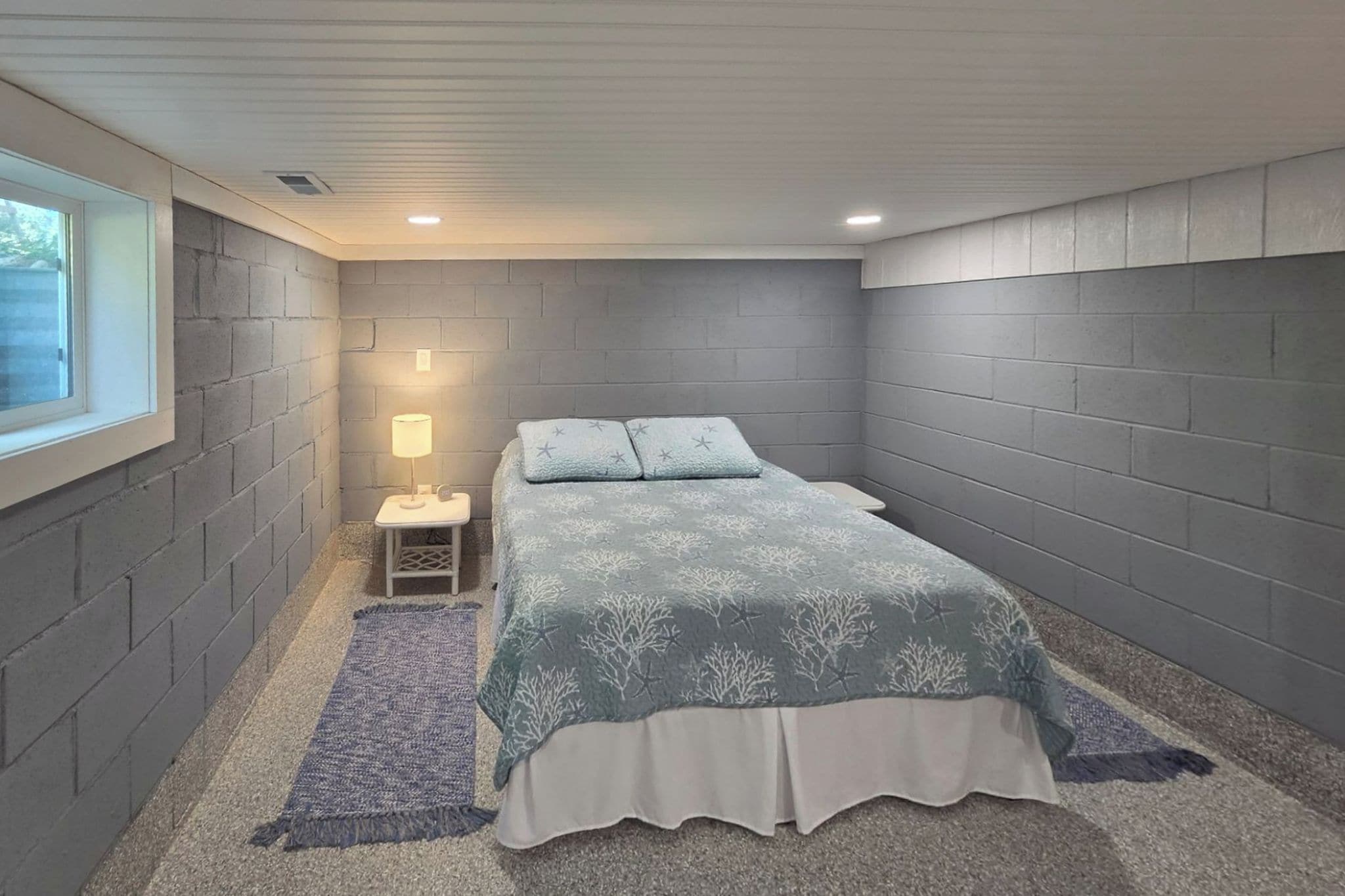 A bedroom with a bed, nightstand, lamp, and a window.