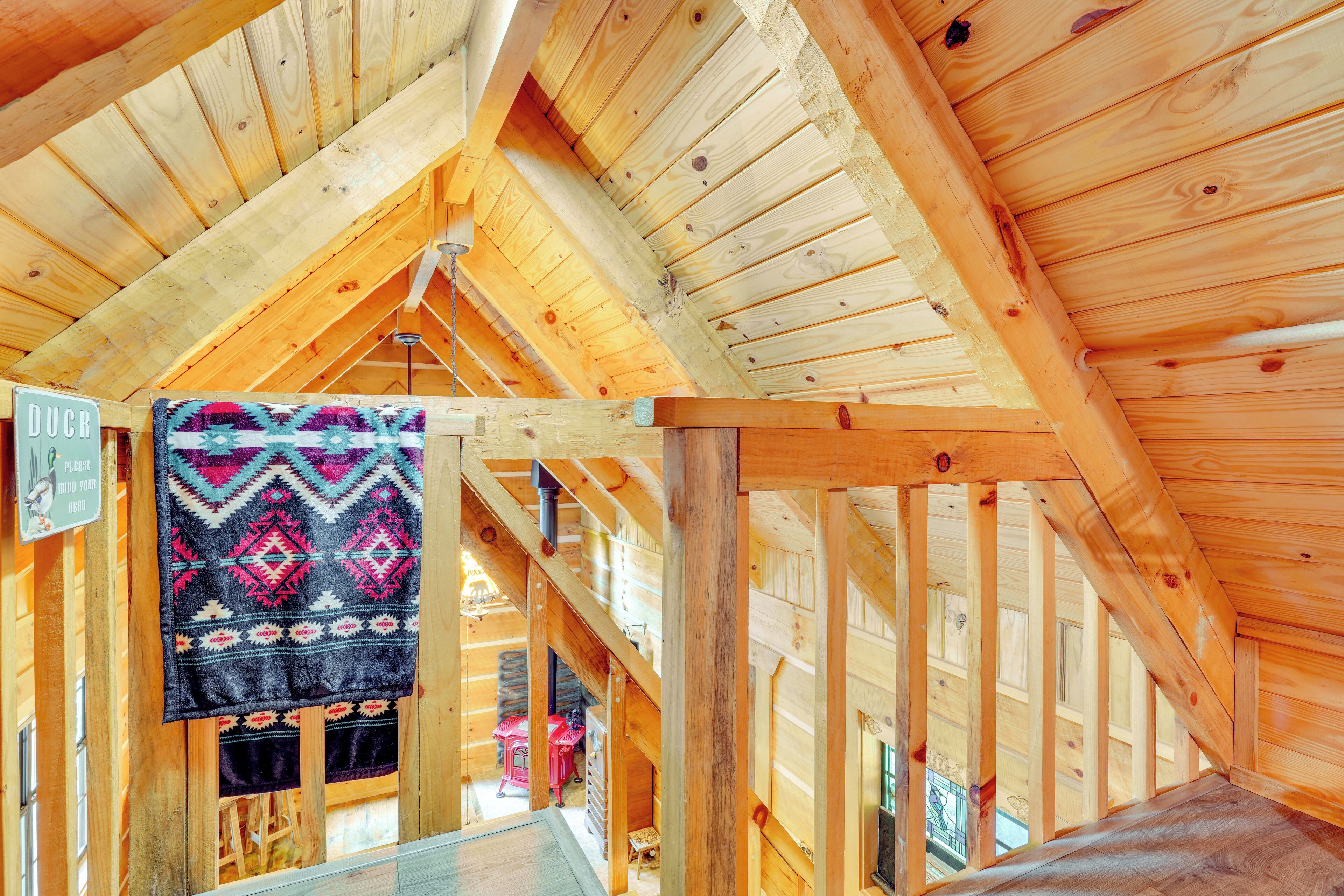 A log cabin interior with a high ceiling, wooden beams, and a patterned blanket hanging on the wall.