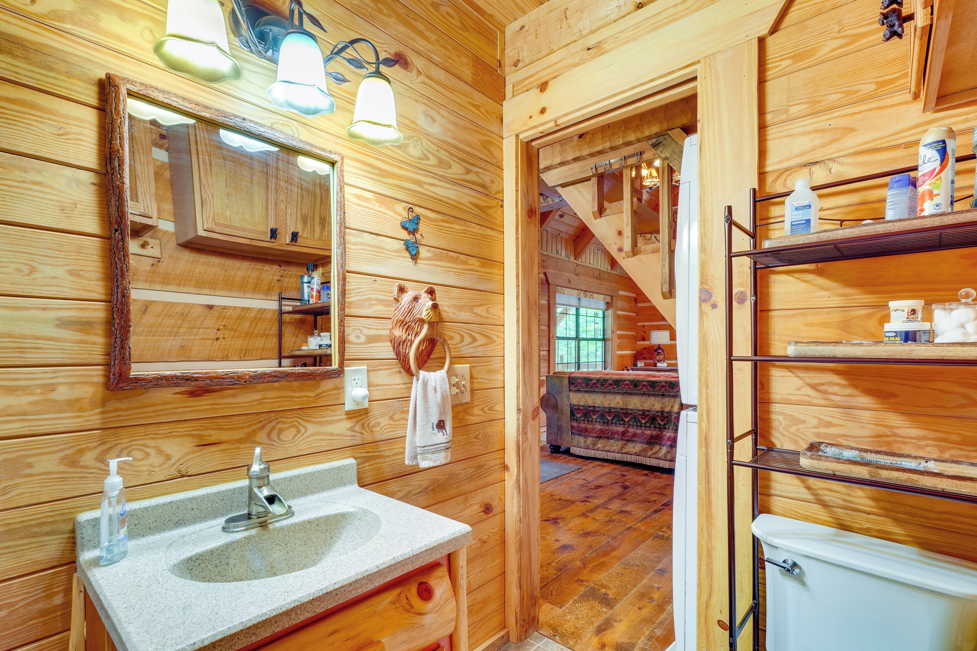 Casa de banho de cabana de madeira, com lavatório, espelho e prateleiras com produtos de higiene pessoal.