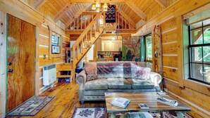 Interior acogedor de una cabaña de troncos con una escalera de madera, un sofá y una mesa de comedor.