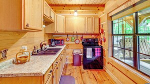 Cocina de cabaña de madera con un ventanal grande, armarios de madera, una estufa y un lavabo.