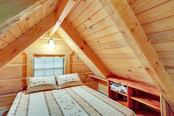 Un acogedor dormitorio en el ático con techo de madera, una cama con ropa de cama a rayas y una peque ña estantería de madera.