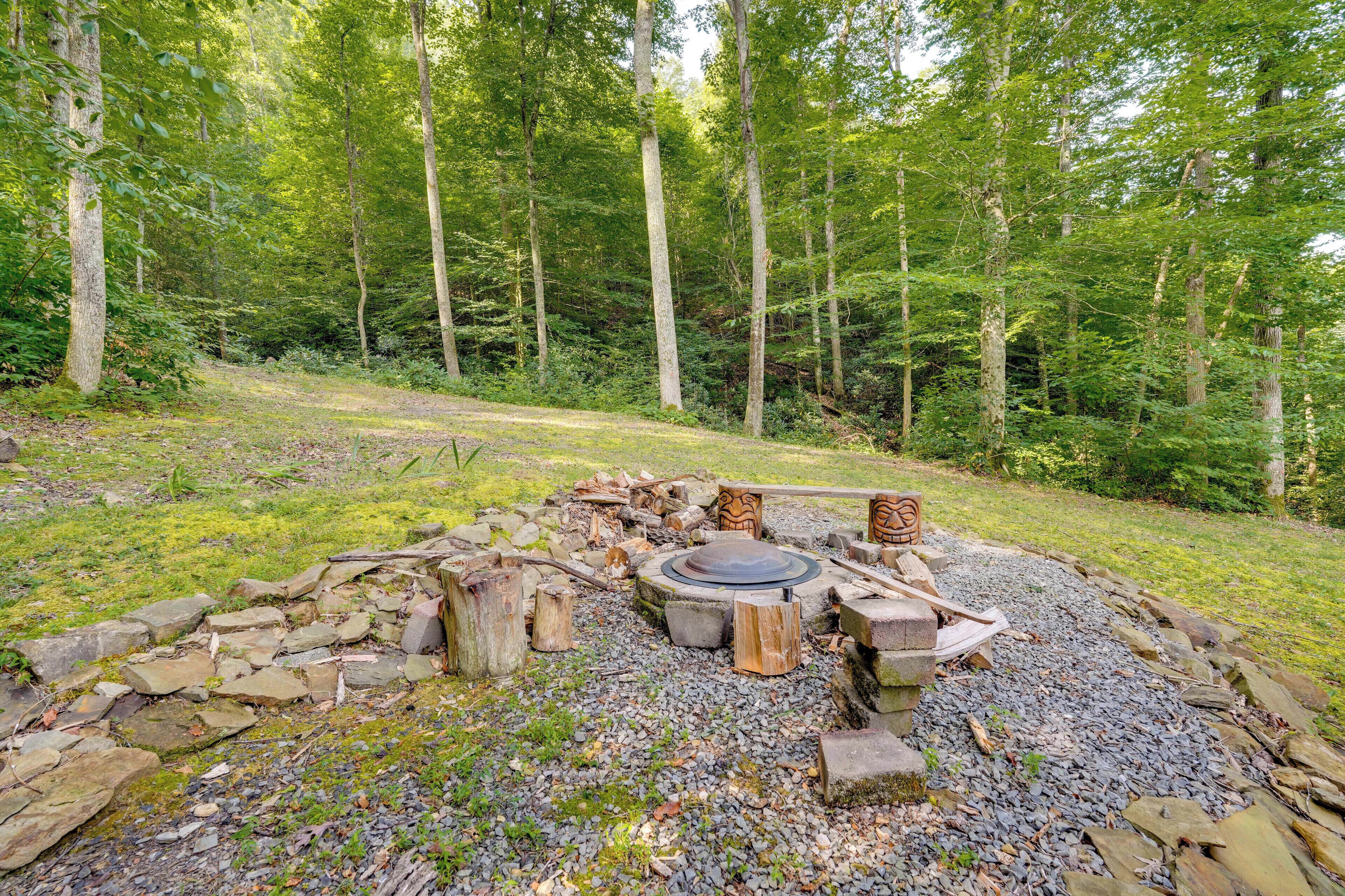 A rustic outdoor fire pit surrounded by rocks and logs in a forested area.
