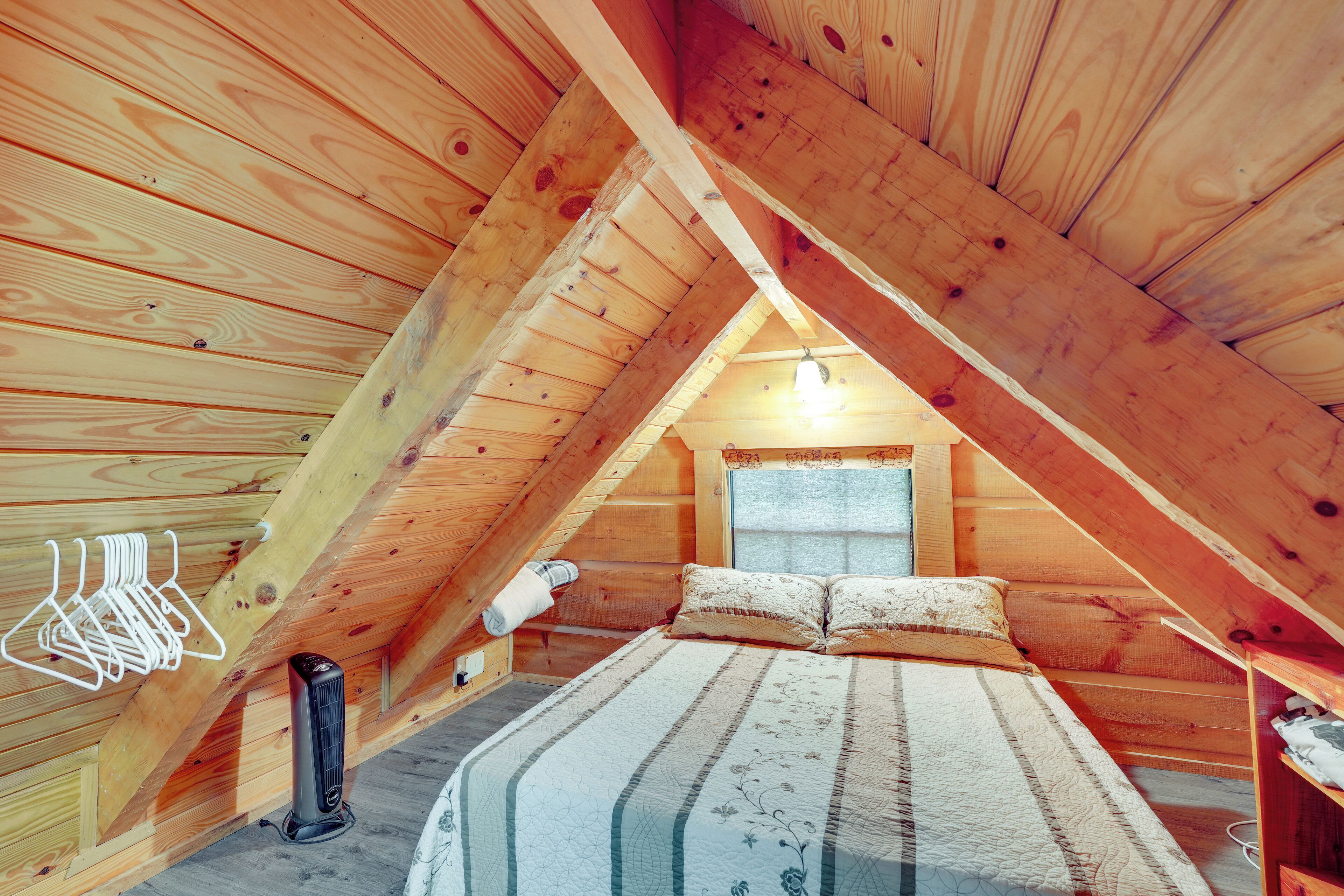 Ein gemütliches Schlafzimmer im Dachgeschoss mit holzgetäfelter Schräge, einem Bett mit gemusterten Betttextilien, einem Heizgerät und einem kleinen Fenster.