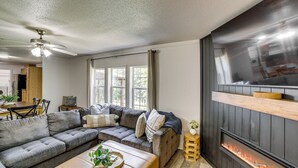 A living room with a sectional sofa, a fireplace, and a ceiling fan. - Fire Pit & Stunning Lake Views: Shell Knob Home! (Shell Knob)