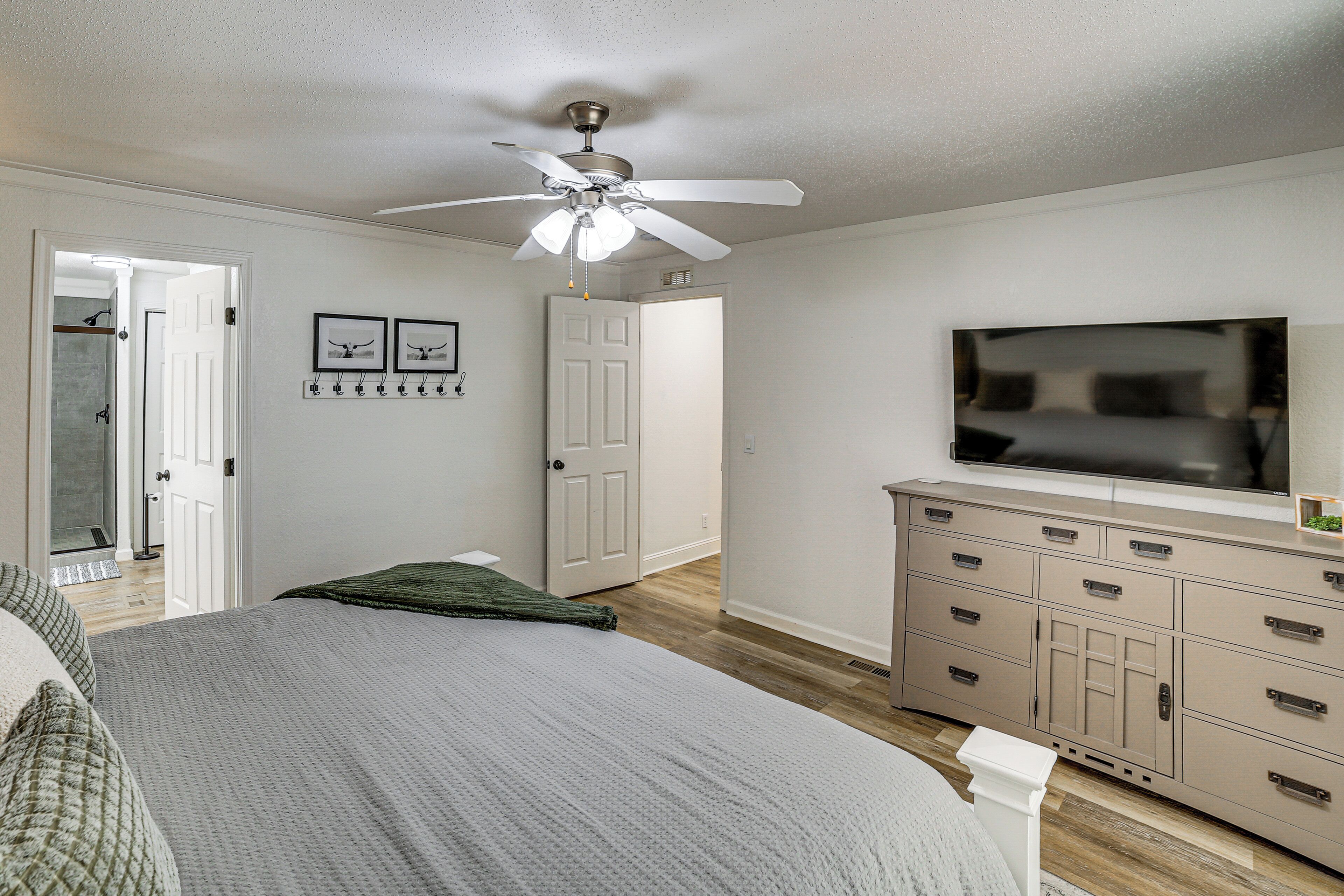 A bedroom with a bed, a ceiling fan, a TV, a dresser, and a door leading to another room.