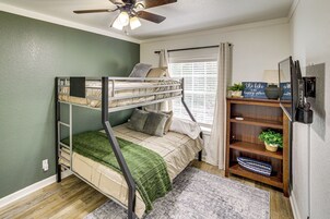Habitación con literas, ventilador de techo, ventana con cortinas, una estantería y una planta pequeña.