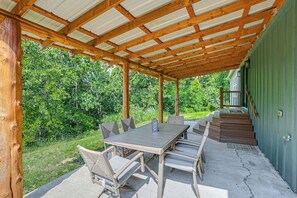 An outdoor covered patio with a wooden table and chairs, a lantern, and a staircase leading to a porch.