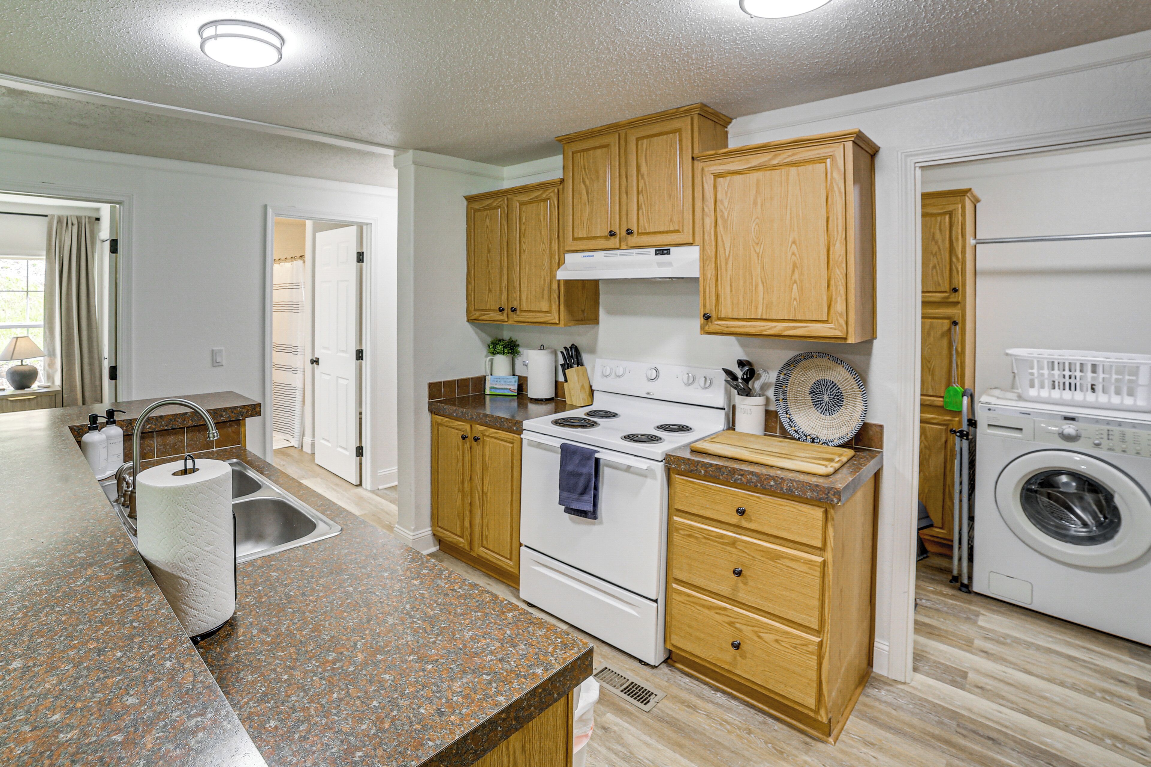 A kitchen with wooden cabinets, a stove, a sink, and a washing machine.