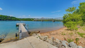A wooden pier extending into a calm river, with a bridge in the background and greenery on the banks. - Fire Pit & Stunning Lake Views: Shell Knob Home! (Shell Knob)